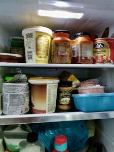 Fridge shelves with yogurt, tinned tuna, jam, garlic, condiments and cold meat